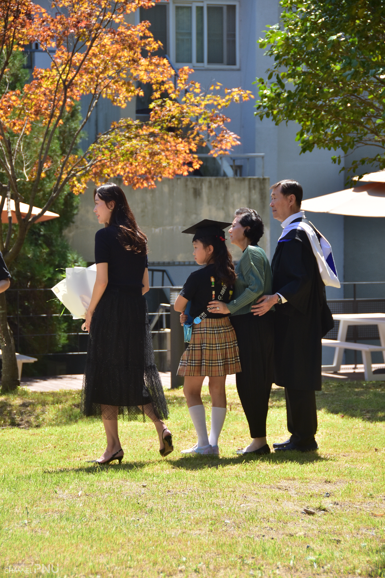 A family is taking the picture. The graduate is the woman leftmost. But her daughter grabs the mortarboard and diploma, and her father wears the graduation gown. [Jun Hyung-Seo, Reporter]