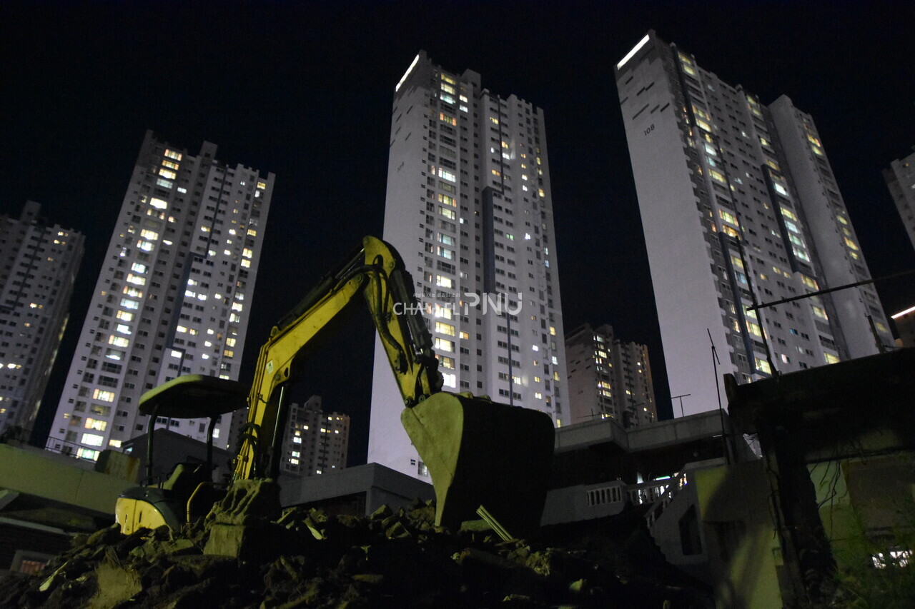 An excavator is neglected on fallen bricks within Jangjeon District 6, with a view extending to the Raemian Jangjeon Apartments. [Cho Young-Min, Reporter]