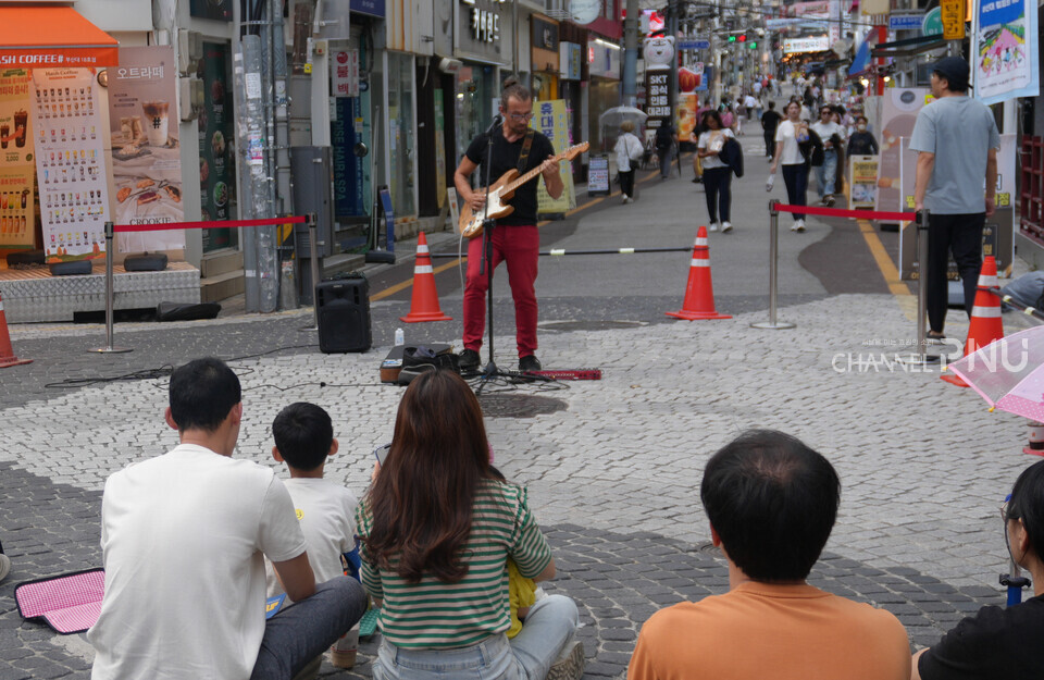 지난 9월 28일 오후 4시경 부산대 젊음의 거리에서 '생생한 루프공연'에 시민들이 주최측에서 마련한 깔개 위에 앉아 연주자의 공연을 관람하고 있다. 공연은 실시간으로 만든 반주 위에 목소리를 이용하여 음악을 번갈아하는 연주이다. [황주원 기자]