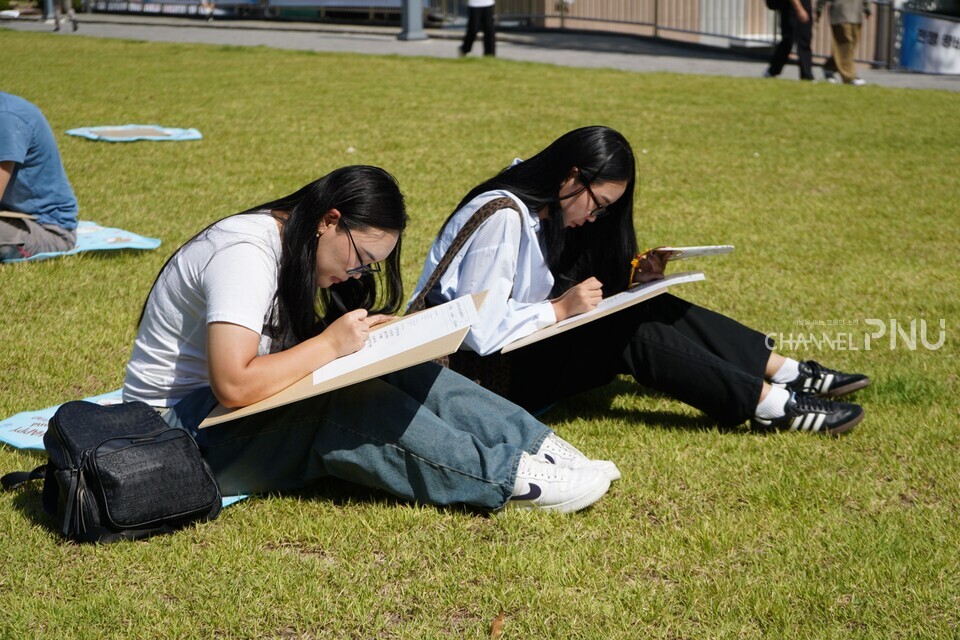 지난 10월 1일 열린 ‘PNU K-Festival’에서 유학생들이 가을 햇살을 받으며 새벽뜰에 앉아 ‘손 글씨 콘테스트’에 참여하고 있다. [김보경 기자]
