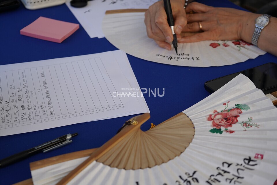 지난 10월 1일 열린 ‘PNU K-Festival’에서 유학생들이 원하는 문구를 전달하면 현장에서 캘리그라피를 완성해 부채에 새겨 준다. [김보경 기자]
