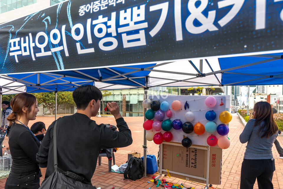 ​지난 10월 30일 우리 대학 시월광장 넉넉한 터에서 진행된 SPOT 연합 축제 부스에서 한 학생이 다트로 풍선을 터뜨리는 게임을 하고 있다. [송민수 기자]